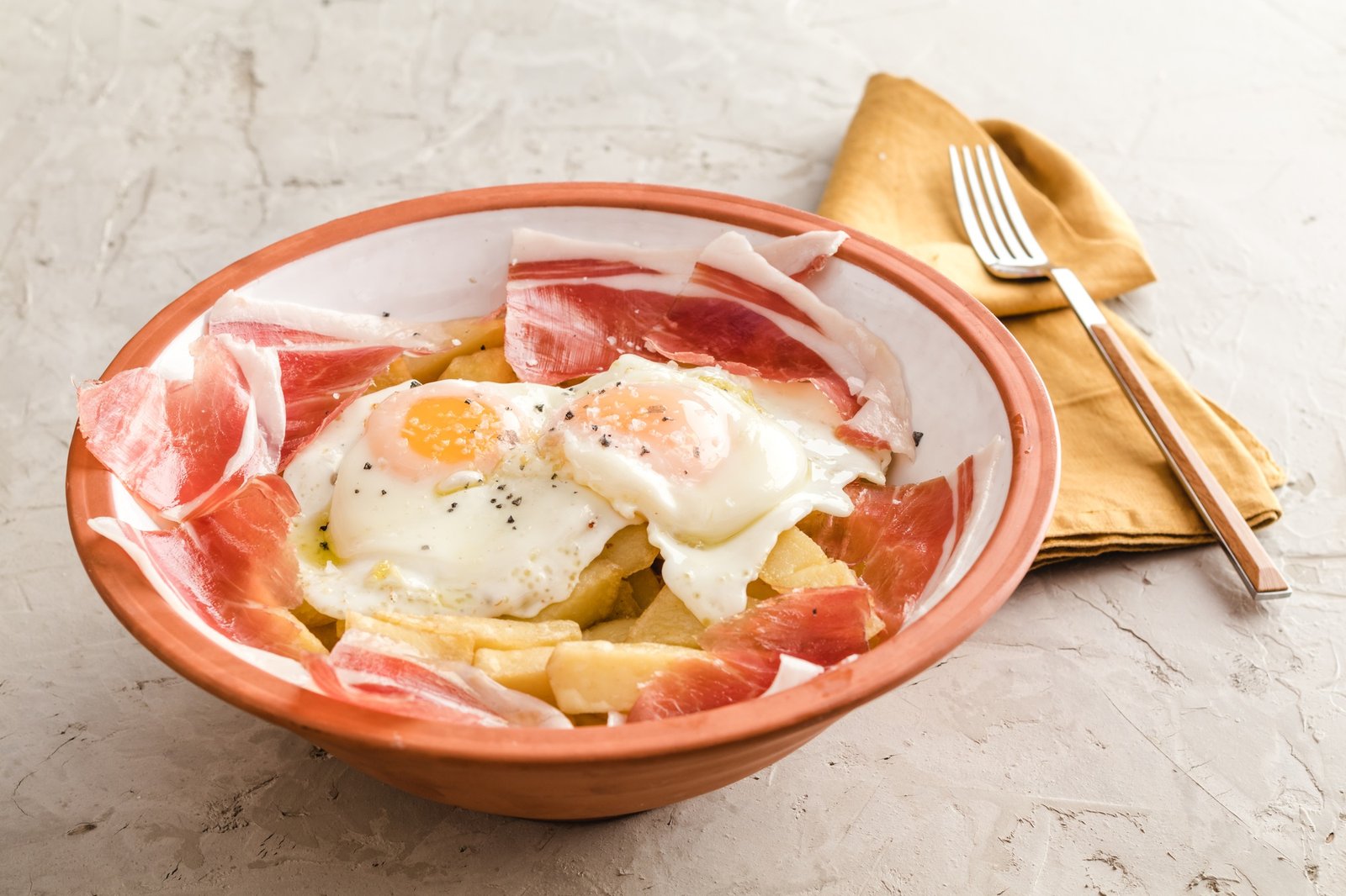 Broken fried eggs with potatoes and Iberian cured ham